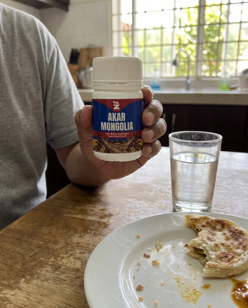 Tangan memegang botol Akar Mongolia di meja sarapan dengan segelas air